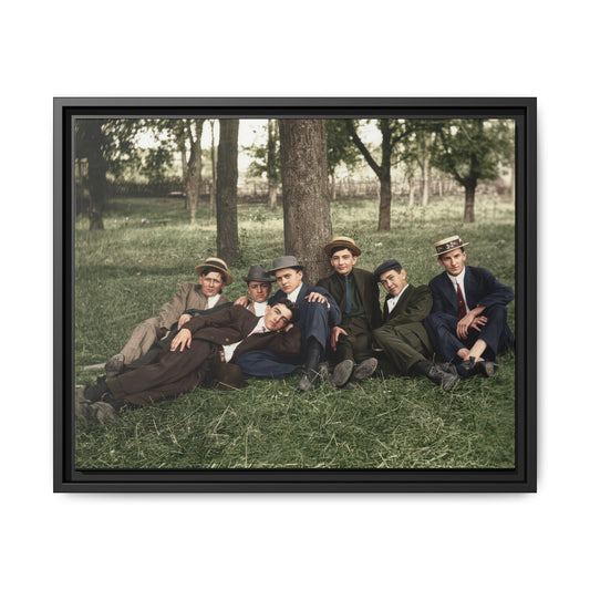 Seven men wearing suits, ties, and assorted hats pose closely outdoors, with one reclining across the foreground.