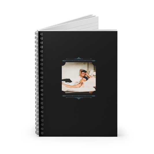 Restored LGBTQ photo of a gay couple resting in bed, featured on a black spiral notebook with vintage flourishes