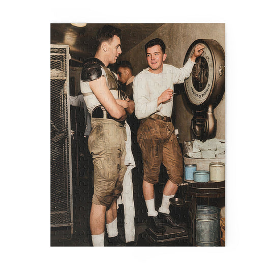 Sideways historical photo of two football players in padded trousers beside a round mechanical scale, with mesh storage and another person partly visible behind them.