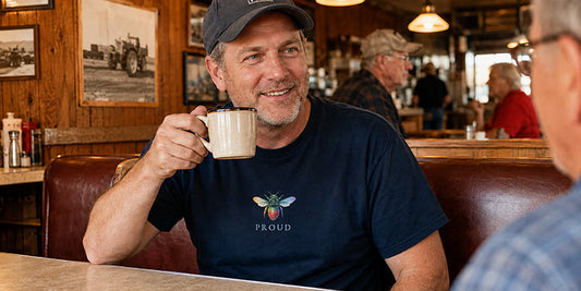 Man wearing a navy Bee Proud LGBTQ+ visibility T-shirt while having coffee and conversation in a vintage American diner