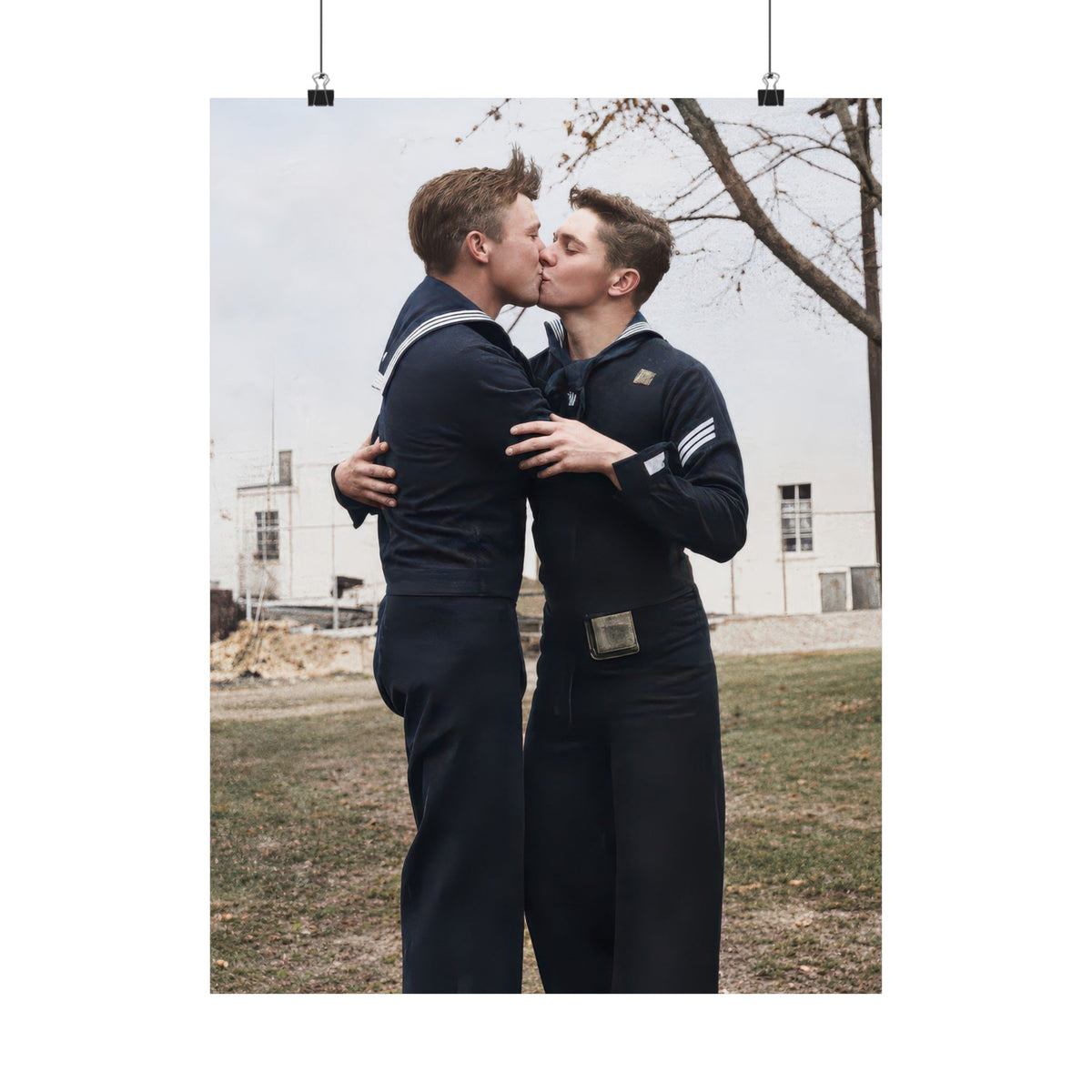 Two men in dark naval uniforms kiss and embrace outdoors beneath a leafless tree, with a pale building in the background.