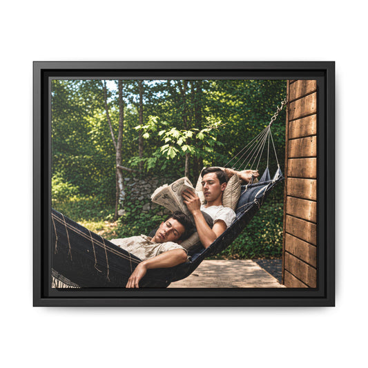 Restored vintage photograph of two men reclining together in a dark hammock, one reading a newspaper, beside a wooden building in a leafy outdoor setting.