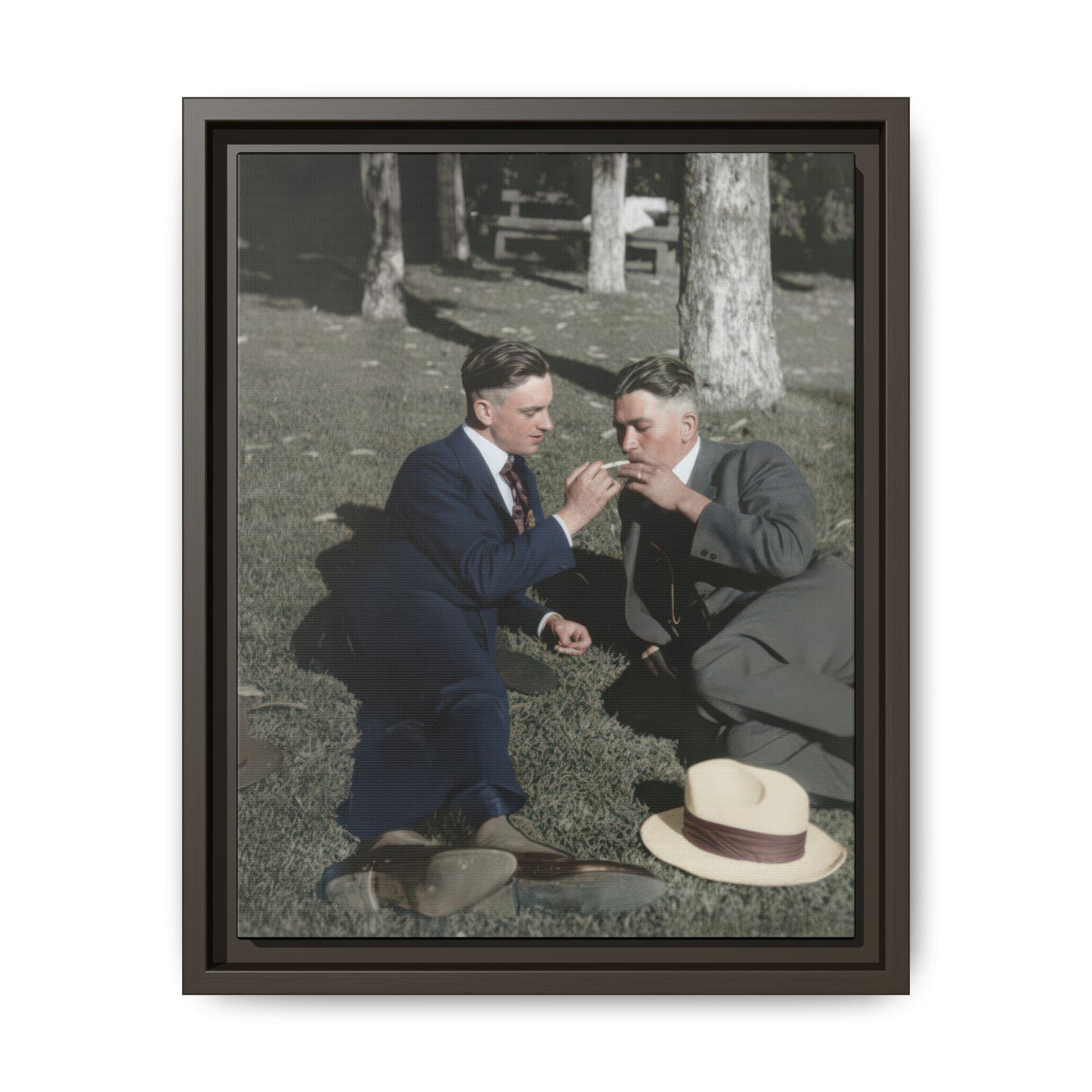 Vintage photograph wall art of two men reclining outdoors with hats on the grass and trees in the background