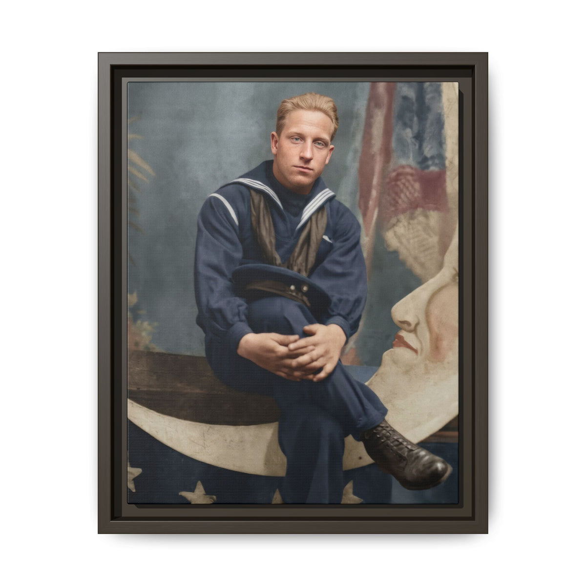 Seated sailor with clasped hands around a raised knee and a cap across his lap, posed on a pale paper moon studio prop.