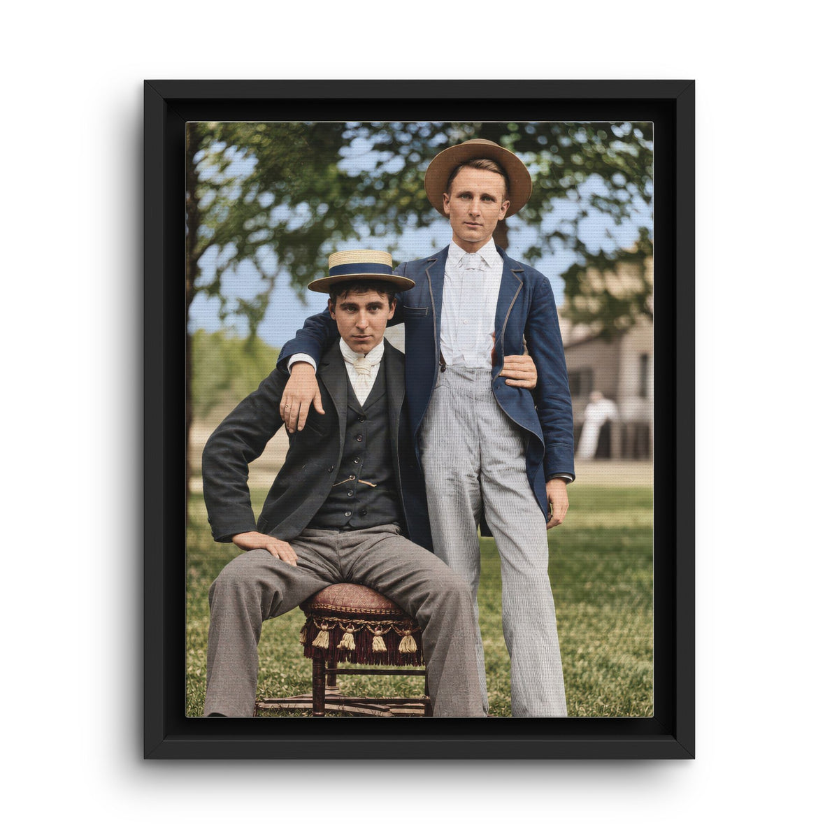 Paire 167 vintage portrait of two men wearing straw hats and tailored jackets, one seated on an upholstered chair outdoors.