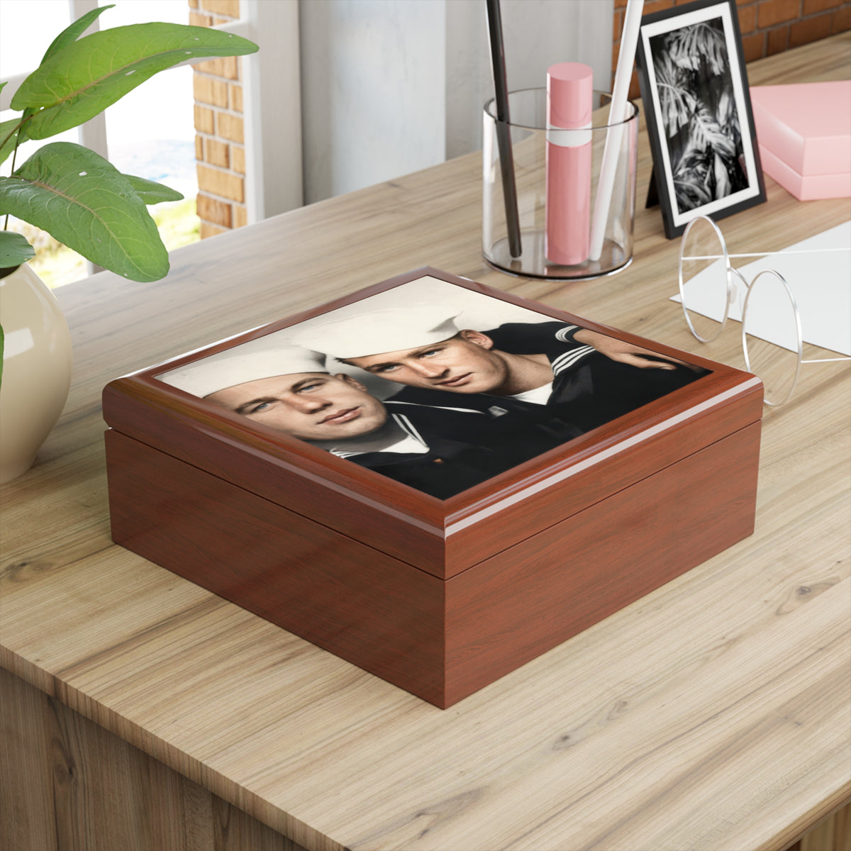 Overhead view of a keepsake box lid showing two sailors in dark uniforms and white caps, with an arm around the shoulders.