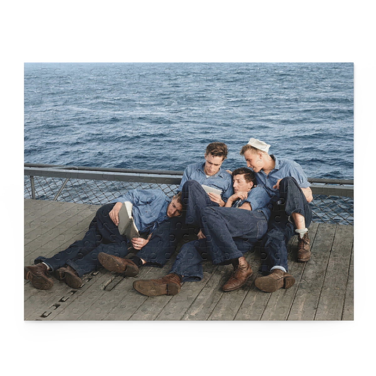 Partly assembled sailor reading photograph puzzle with an open book, white cap, worn shoes, and mesh deck barrier.