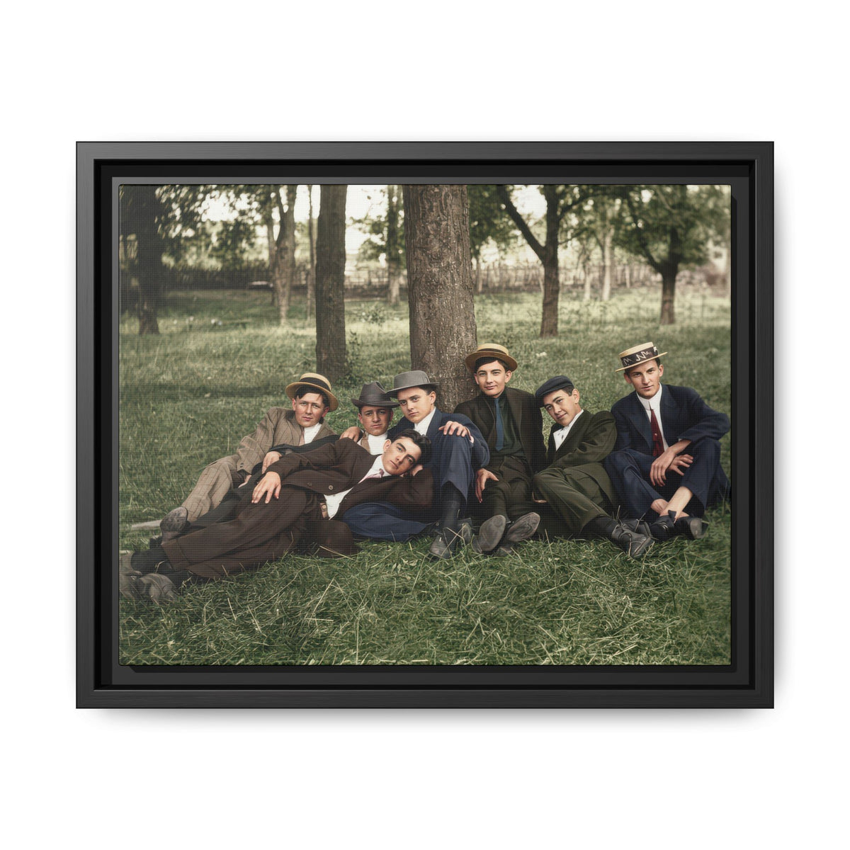 Restored historical photograph of seven men in suits seated and reclining on grass beneath mature trees.