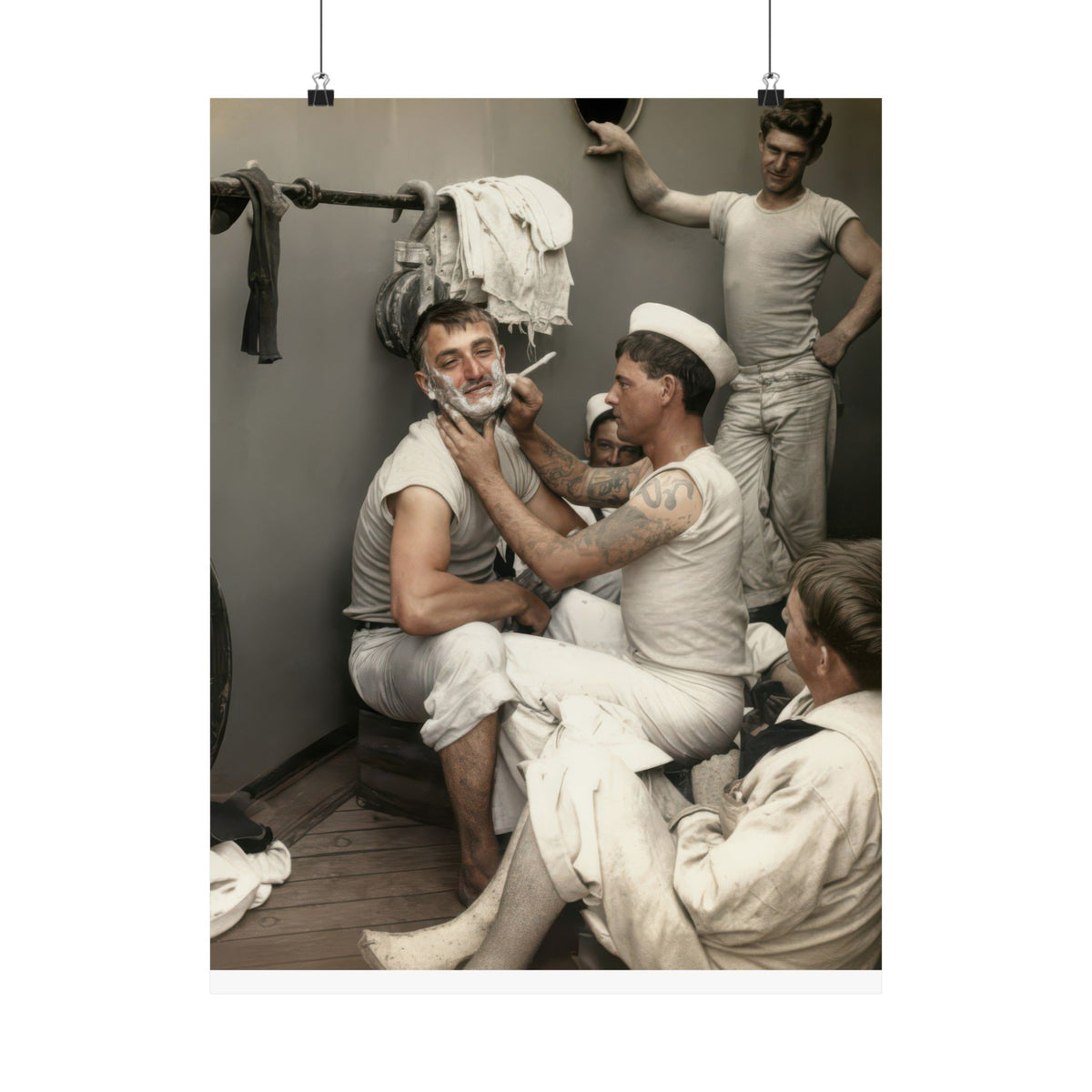 Tattooed sailor shaving a seated man’s lathered face while three other men gather around them in a shipboard interior, circa 1935–1945.
