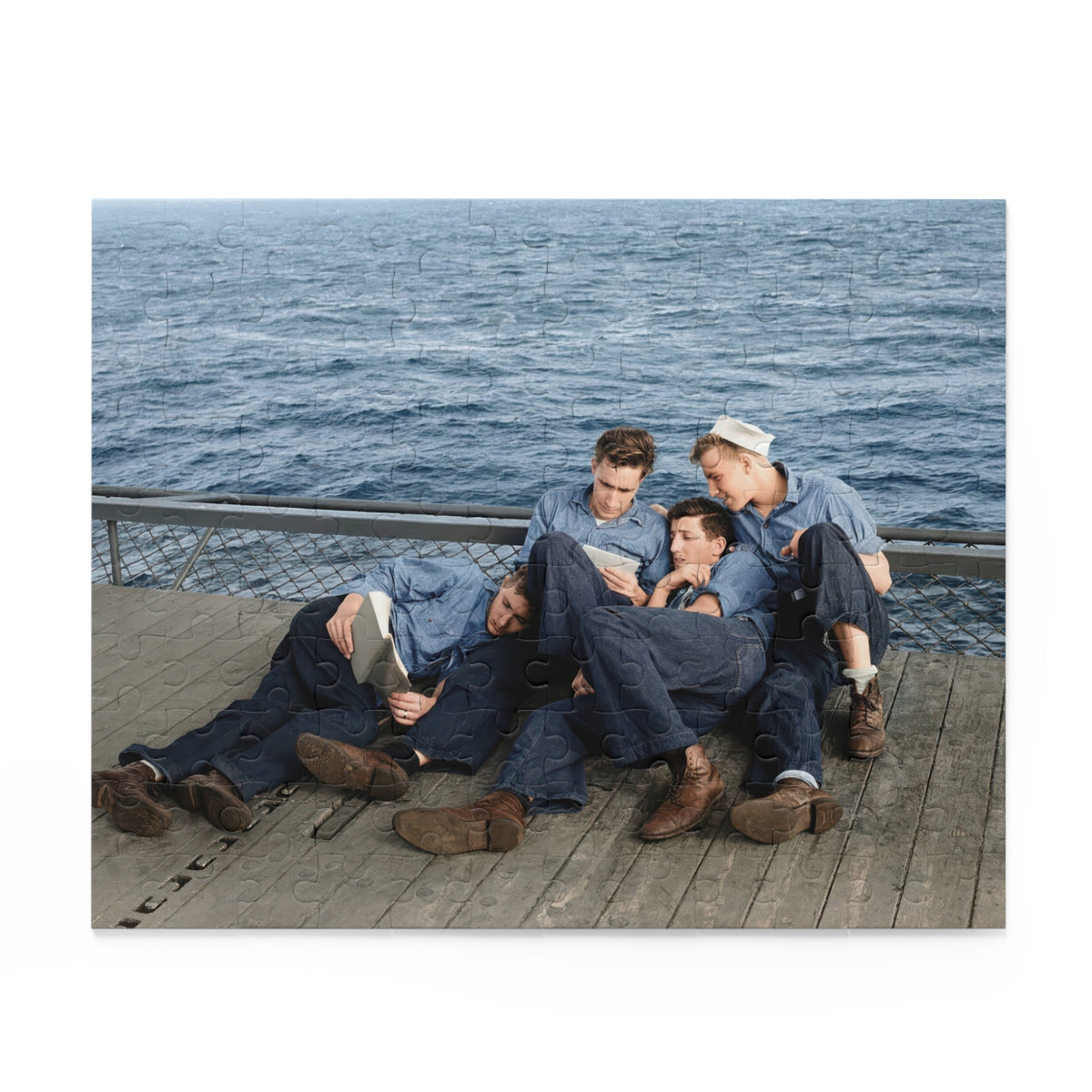 Source artwork for a jigsaw puzzle showing four sailors reading on a wooden deck beside a mesh barrier and open water, with blue shirts and one white cap