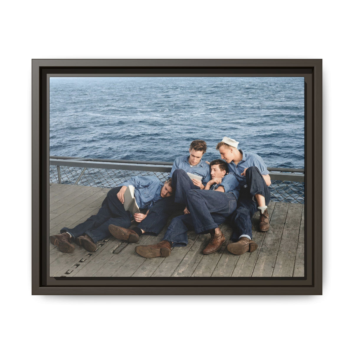 Horizontal historical photograph of sailors reading, with cuffed trousers, worn shoes, and wooden deck planks in the foreground.