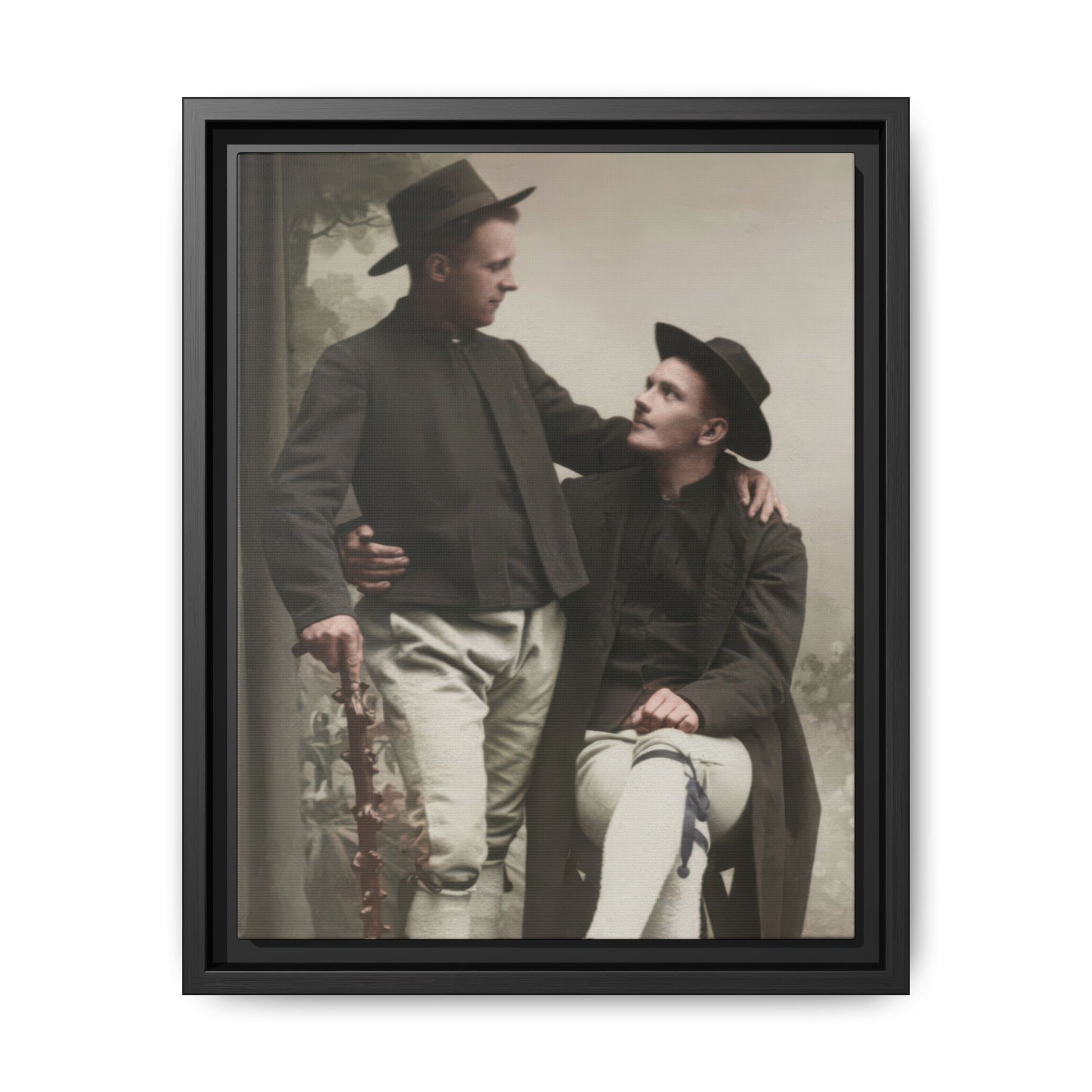 Vintage studio double portrait of two men in hats and dark jackets with one seated and one standing holding a walking stick
