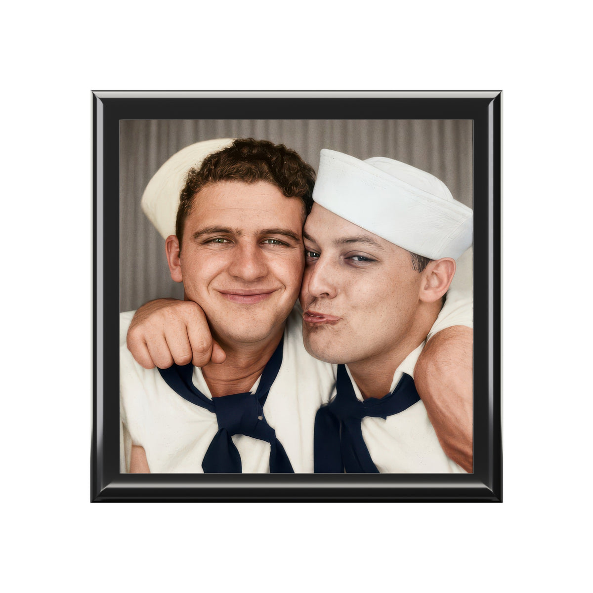 Vintage photobooth portrait of two sailors in white caps, one smiling and the other puckering his lips, with arms around each other.