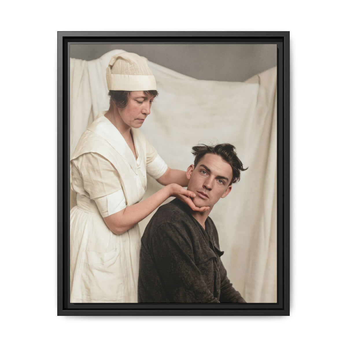 Standing nurse in a pale cap looking downward while the seated man tilts his head and looks toward the camera.