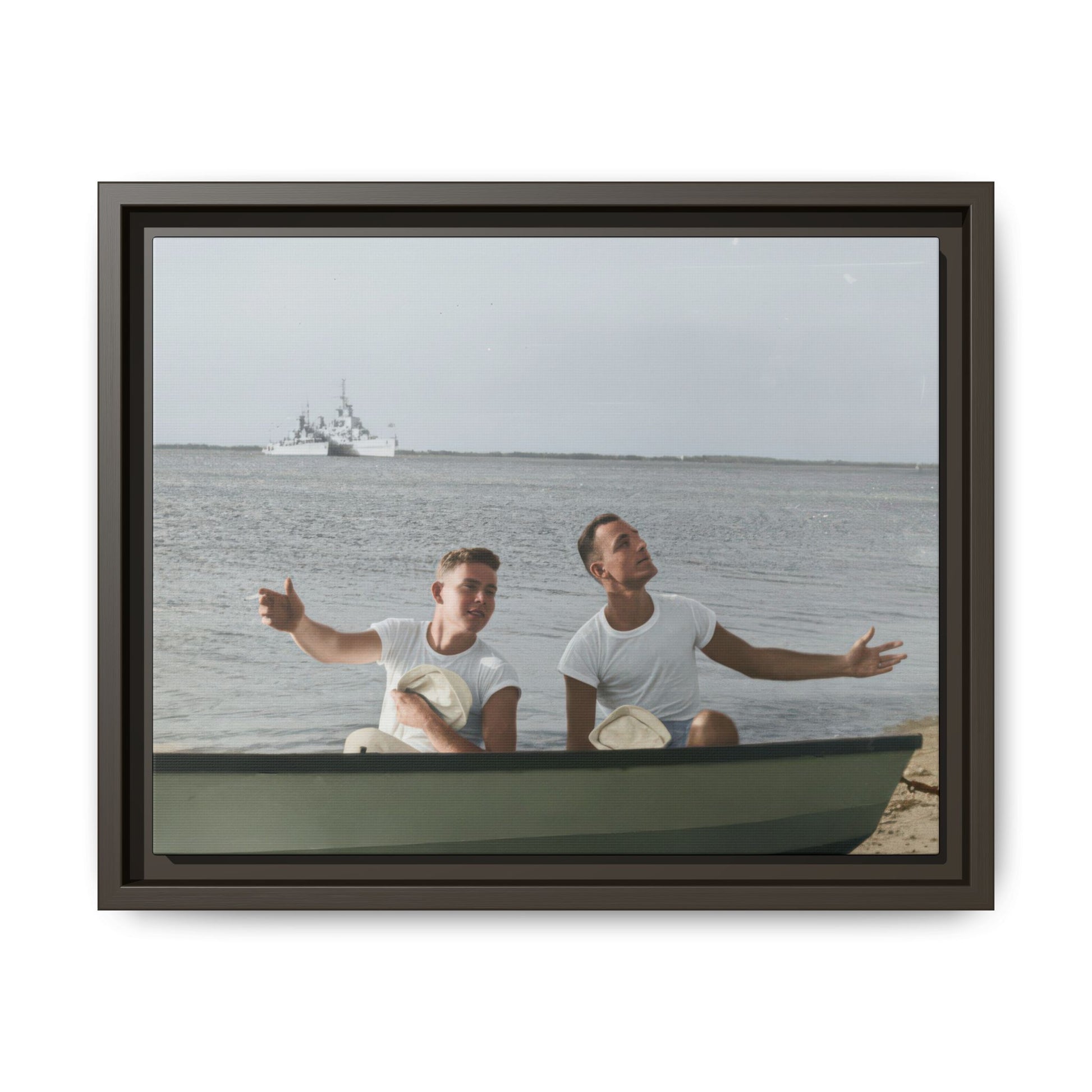 Mid-century outdoor portrait of two sailors seated together in a boat beside a waterfront shoreline