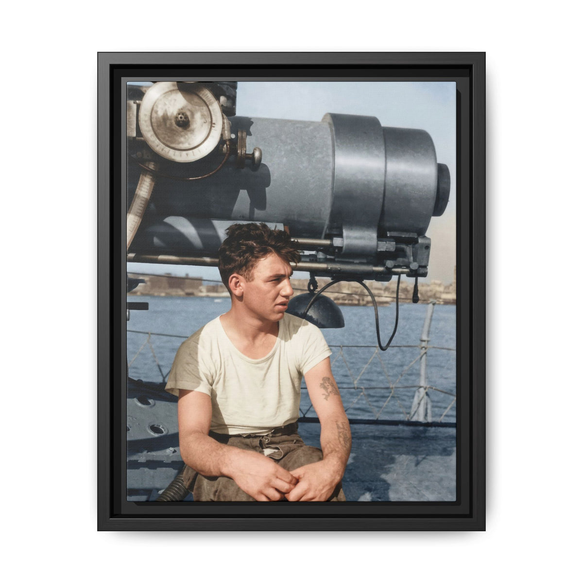 Colorized historical portrait of a tattooed man in a pale shirt and brown trousers, seated beneath shipboard equipment with rope railings and water behind him.