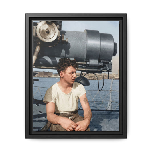 Colorized historical portrait of a tattooed man in a pale shirt and brown trousers, seated beneath shipboard equipment with rope railings and water behind him.