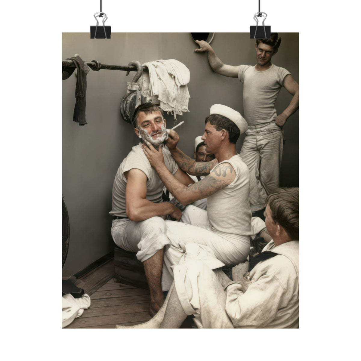 Restored historical naval photograph featuring a white sailor cap, tattooed arms, hanging towels, and wooden deck boards.