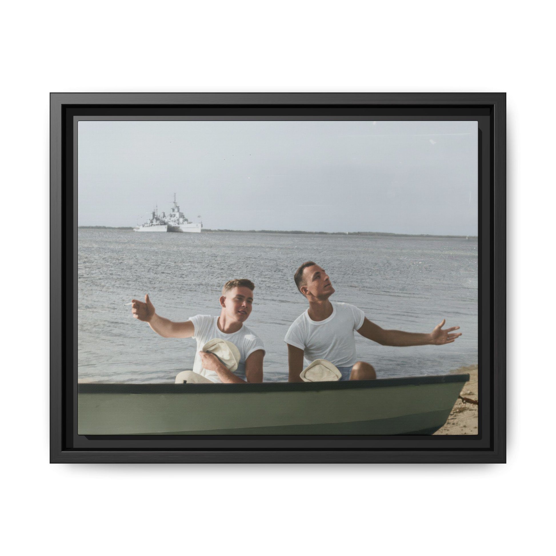 Vintage photograph of two sailors seated in a small boat near shore with a warship in the distance