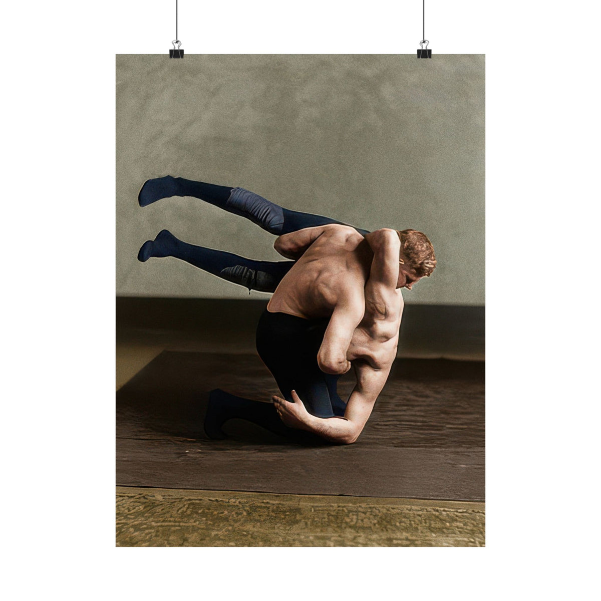 Two male wrestlers demonstrating a shoulder-carry grappling position on a padded studio floor, circa 1910–1920.