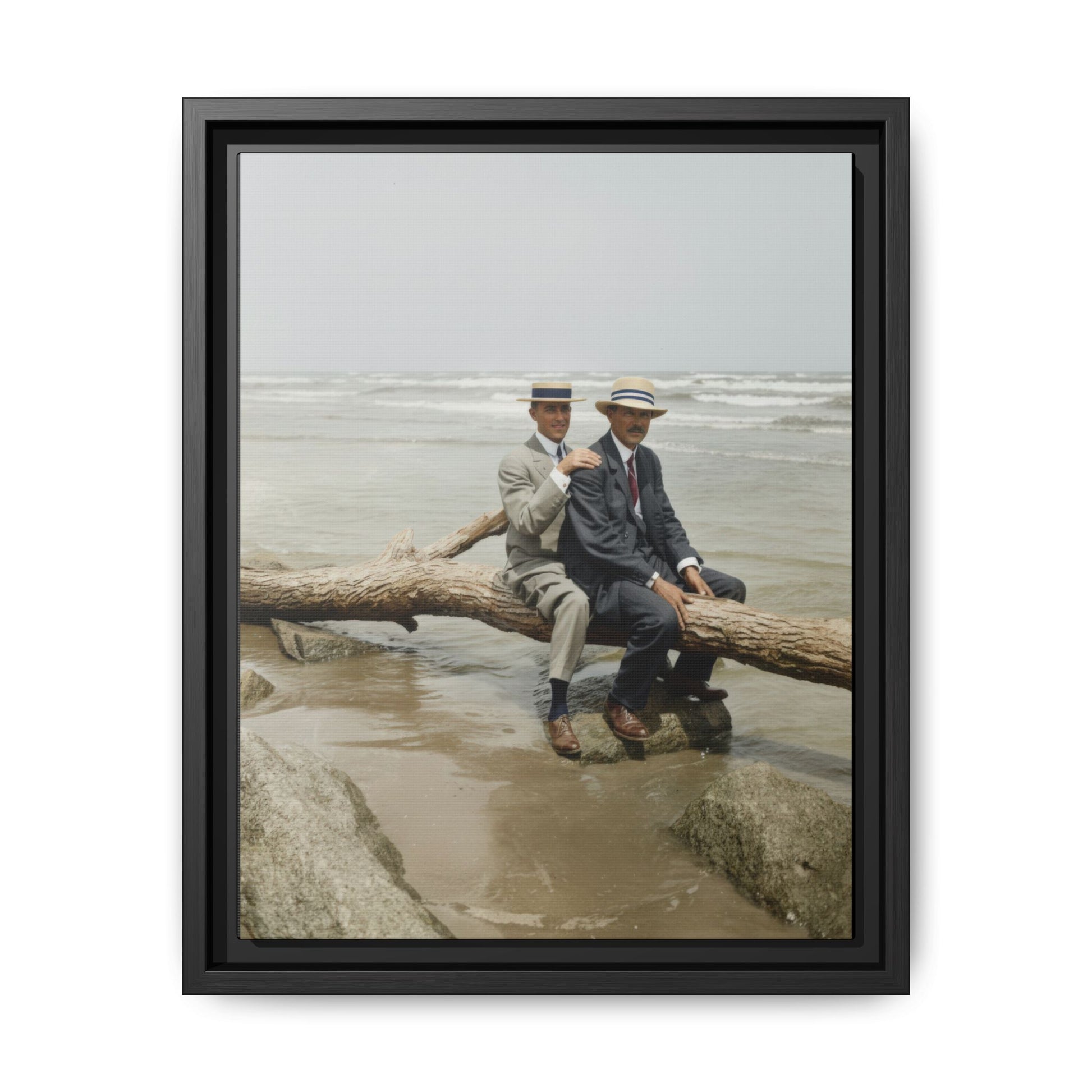 Early 20th century seaside portrait of two men seated on driftwood log wearing straw boater hats