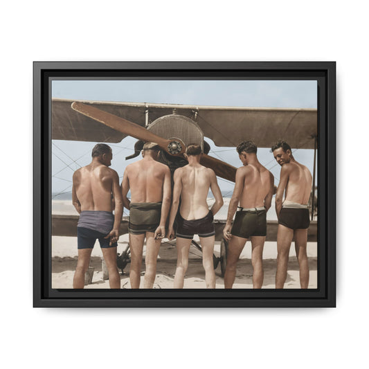 Restored colorized photograph of five bare-chested men in short trunks, seen from behind before a biplane on sandy ground.