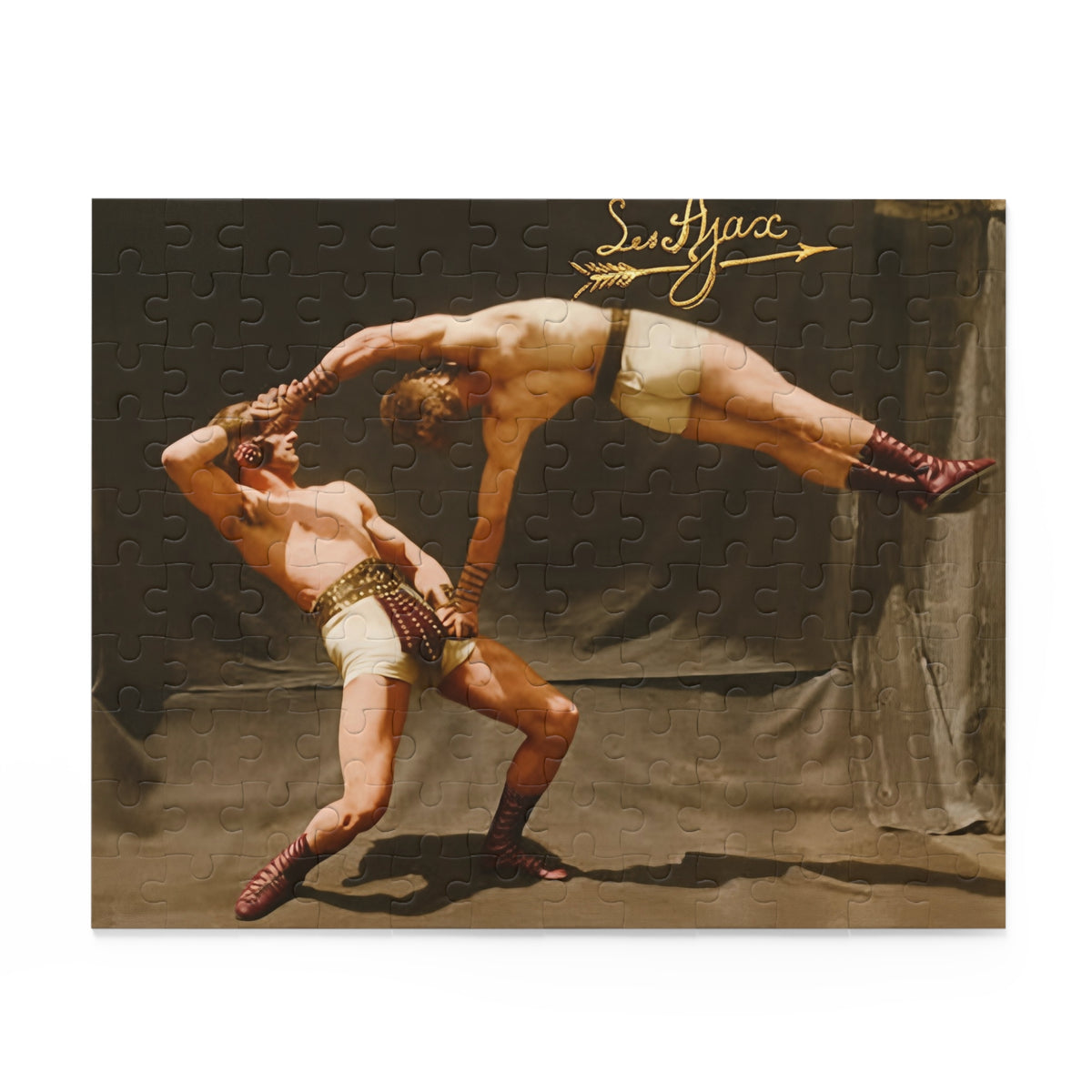Two Les Ajax acrobats in cream costumes and burgundy boots perform a counterbalance lift before drapery, beneath a gold script inscription and arrow