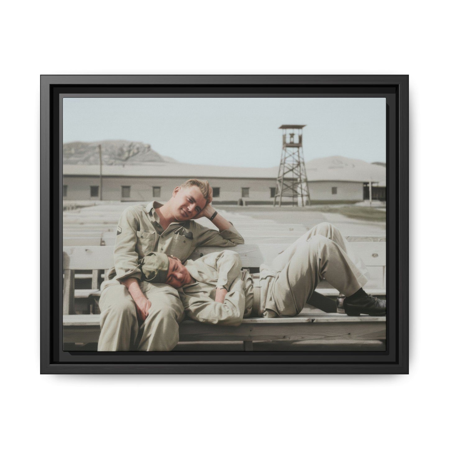 Vintage photograph of two soldiers resting on wooden benches at a military base with a watchtower in the background